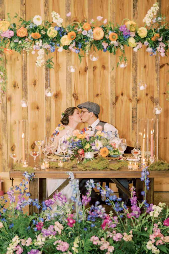 Bride and groom kissing under floral installation with hanging candles